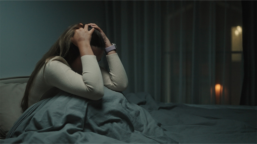 Young Asian woman sits up in bed in middle of the night distraught