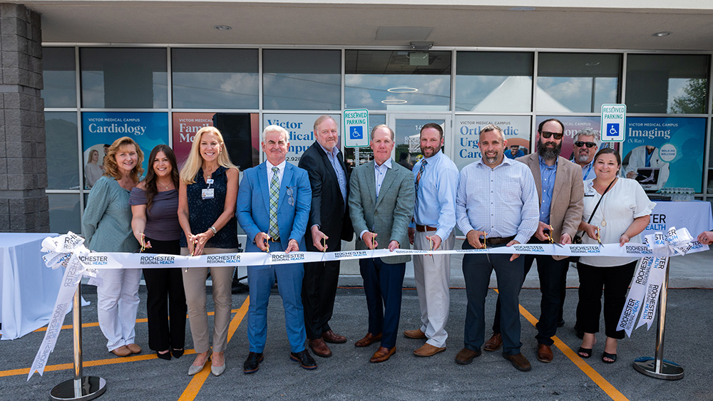 Group of men and women in business attire smiling and cutting ribbon using golden scissors
