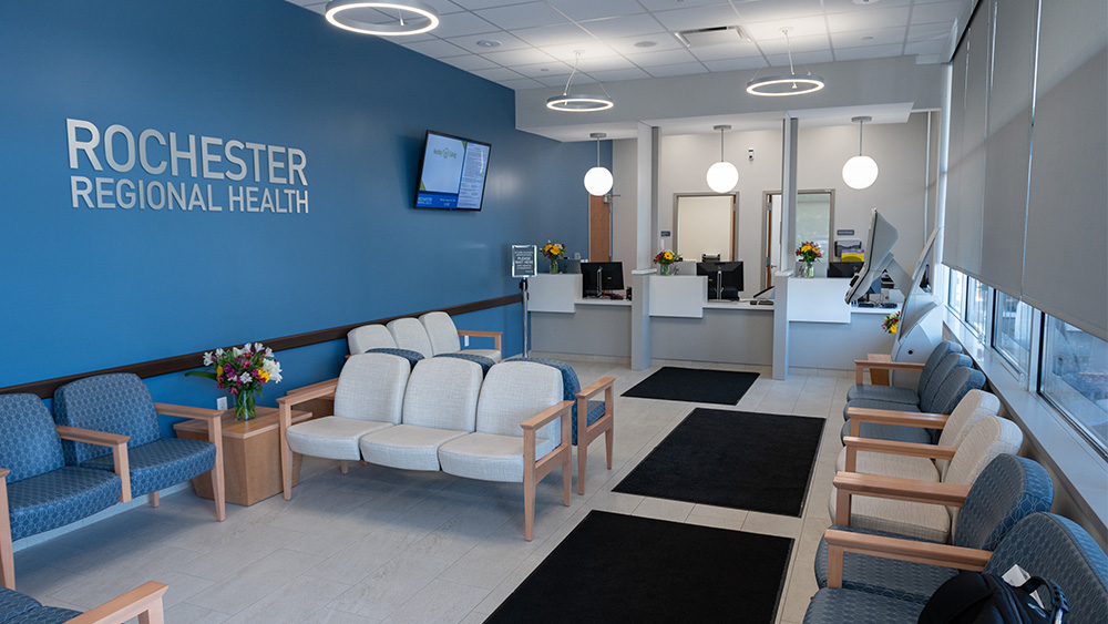 Medical campus waiting room with blue walls white chairs a reception desk and calming lighting