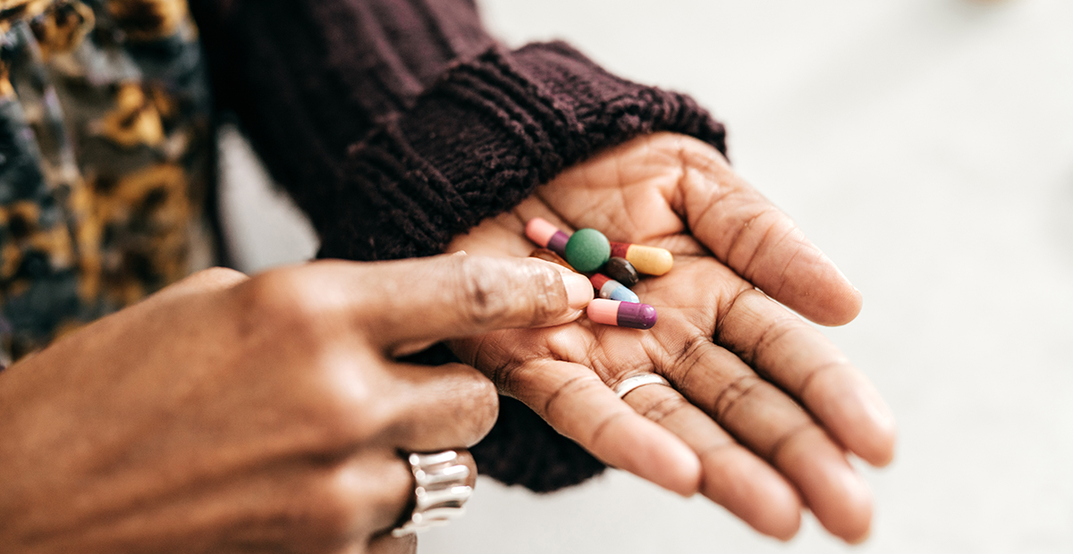 Black woman in brown sweater holds vitamins and supplements in palm of her hand