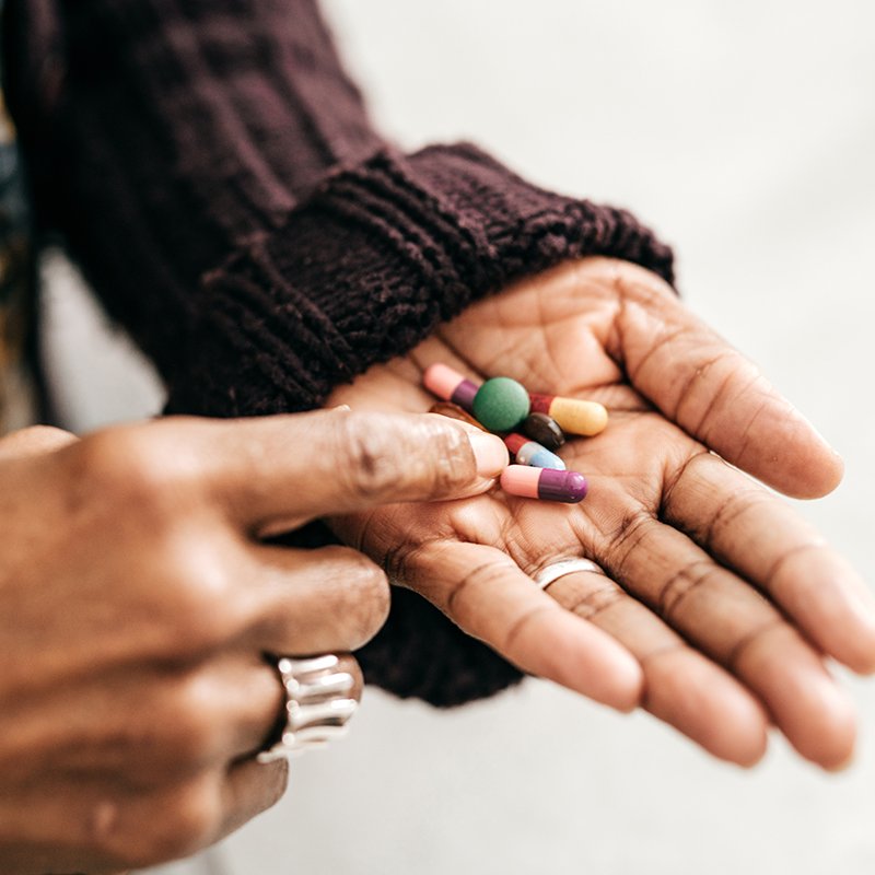 Black woman in brown sweater holds vitamins and supplements in palm of her hand