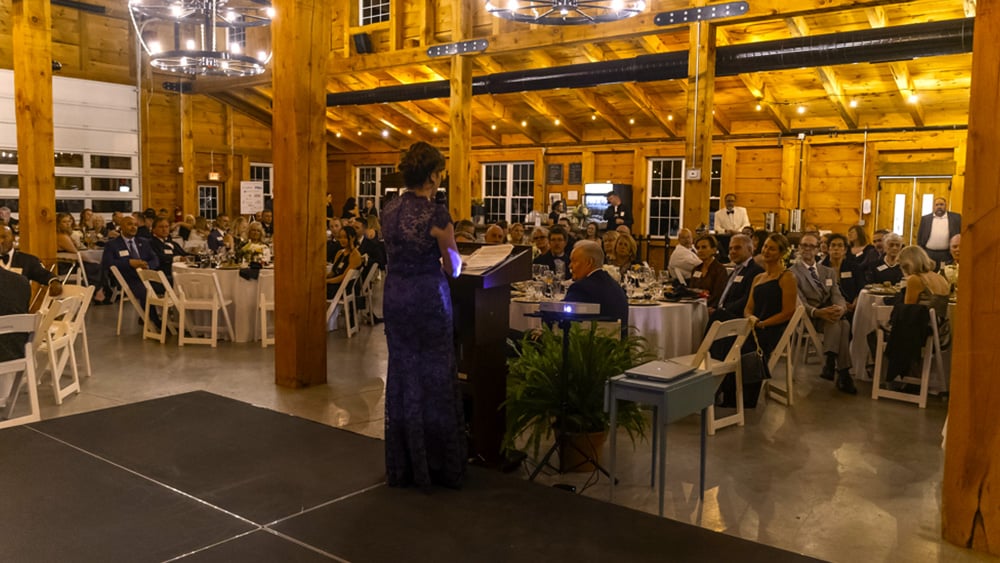 Woman in formal gown talks to room full of formally dressed fundraisers at event