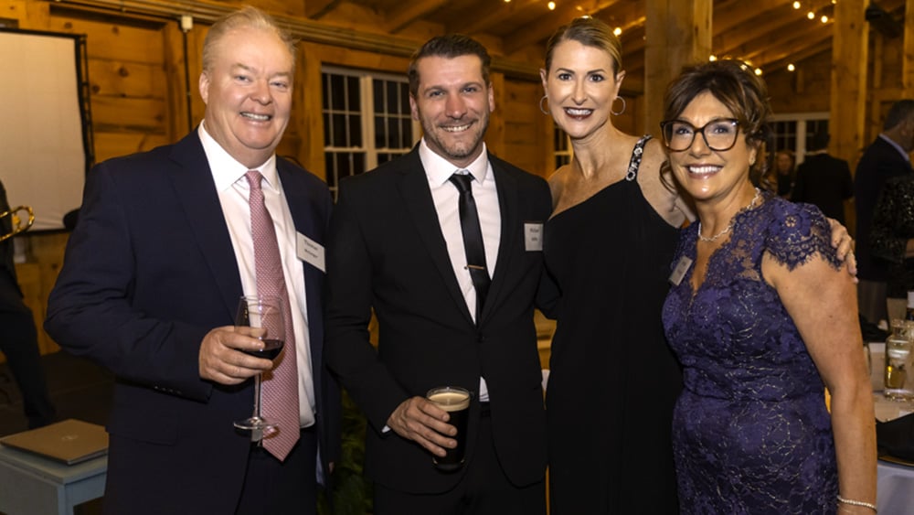 Four adults in formal attire smile at fundraising event