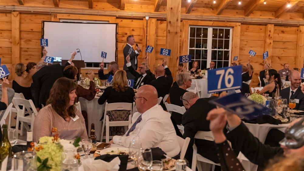 Group of formally dressed adults holding up auction paddles at fundraising event