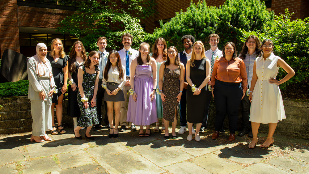 Group of people smiling for group photo in front of trees and a building