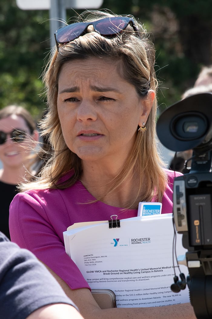 Woman with sunglasses on top of her head in pink shirt talks with media