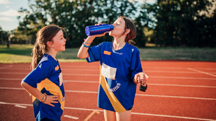 Two female athletes rest and drink water on a running track