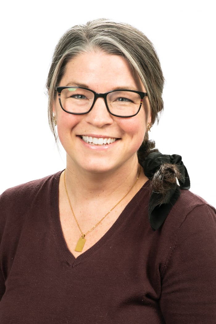 White woman with glasses in maroon v neck sweater smiles for portrait