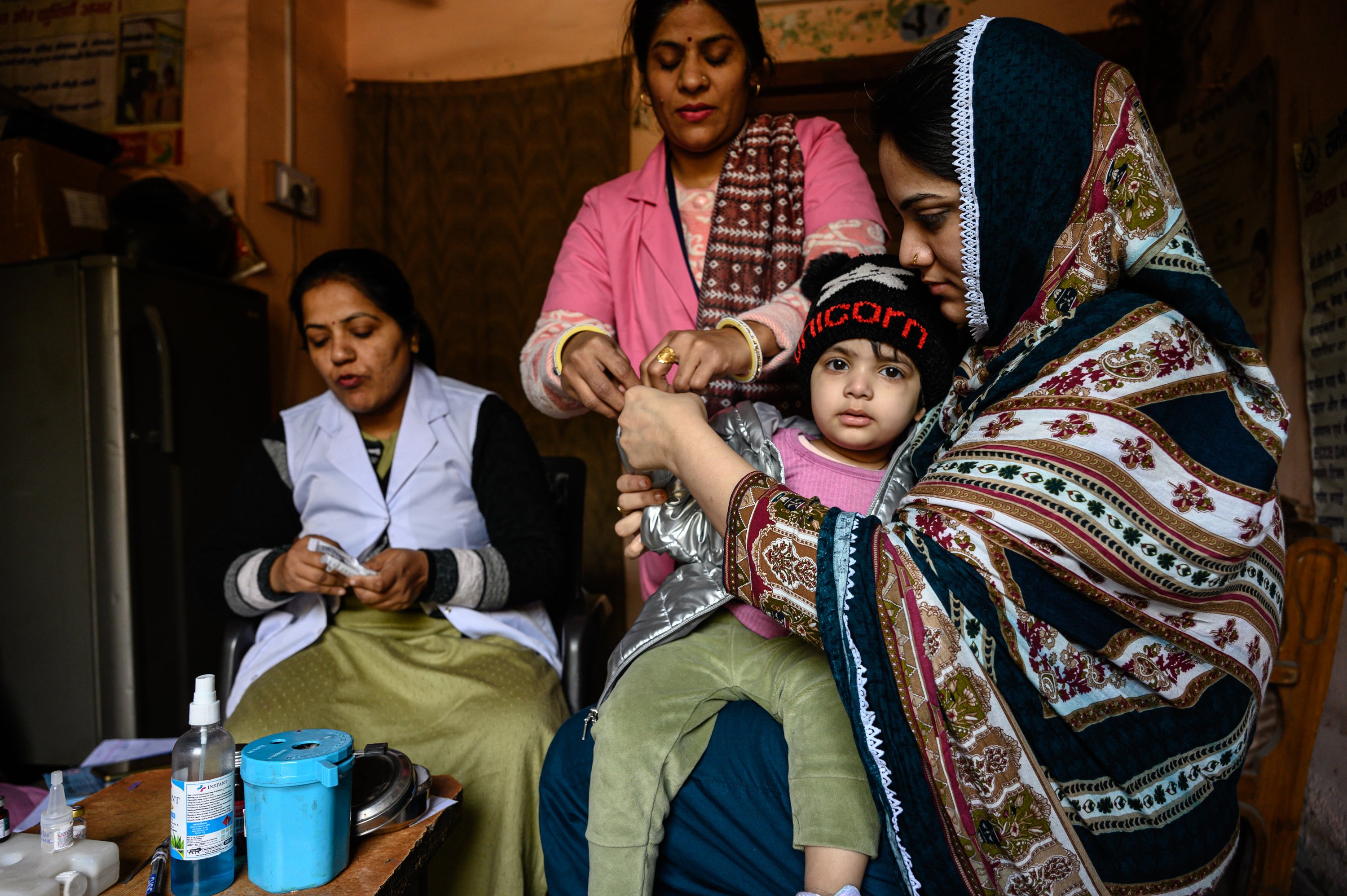 At an Anganwadi community health center in New Delhi, India, a health worker vaccinates a child while caregivers look on