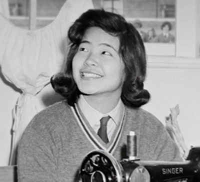 Black and white photo of Yoko Sekimoto smiling, wearing a cardigan with a badge