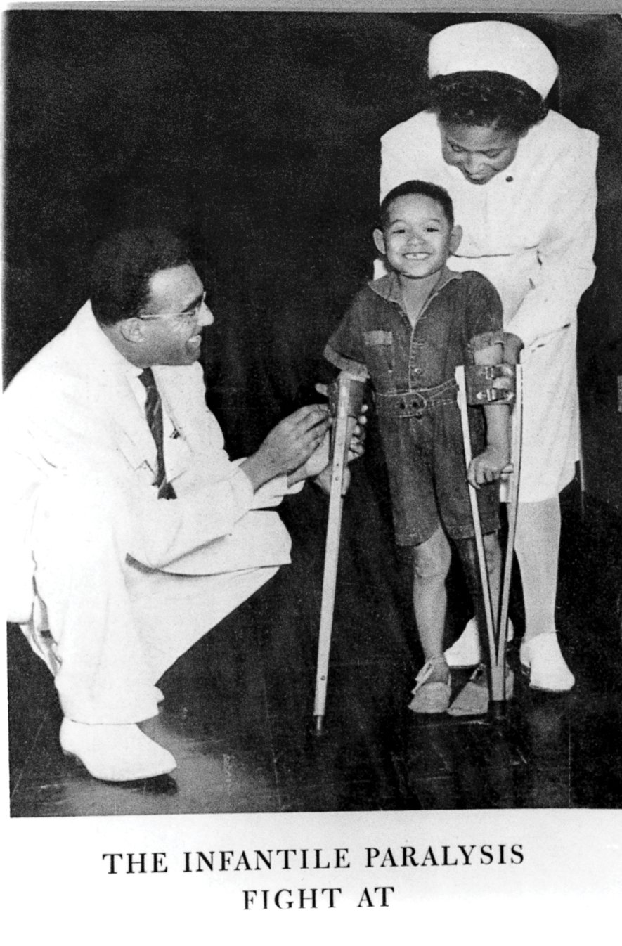 Ein Schwarz-Weiß-Foto, auf dem John Chenault sich bückt, um nach einem Polio-Patienten auf Krücken zu sehen.