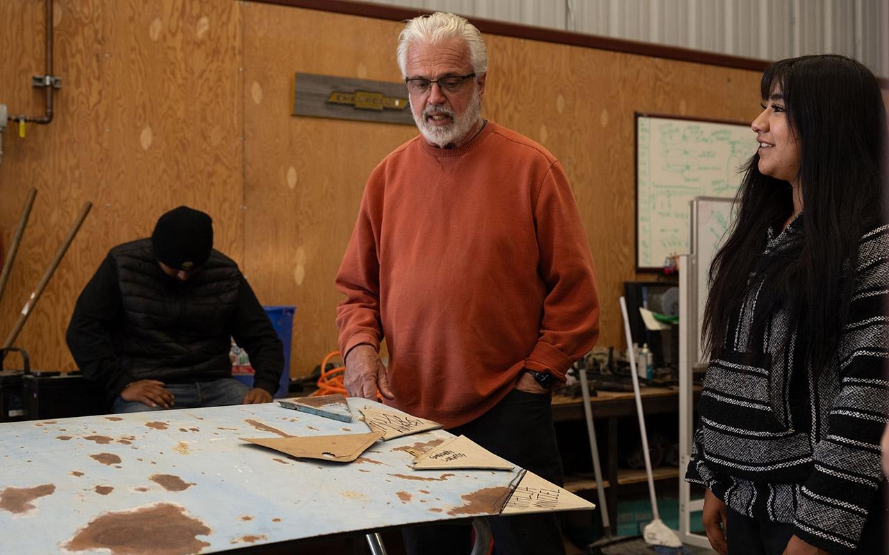 Tom Forgette e outros alunos estão em volta de uma mesa de trabalho coberta de peças de molde, em uma oficina ou sala de aula.