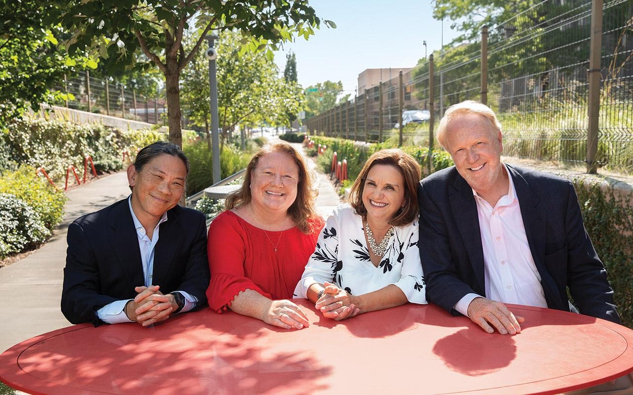 from left) Warner Huh, a gynecological oncologist who chairs the OB-GYN department at the University of Alabama at Birmingham; Nancy Wright, director of the Cancer Prevention and Control Division of the Alabama Department of Public Health; Scarinci; and Bruce Rogers, president of the Rotary Club of Birmingham seated around a red table outdoors.