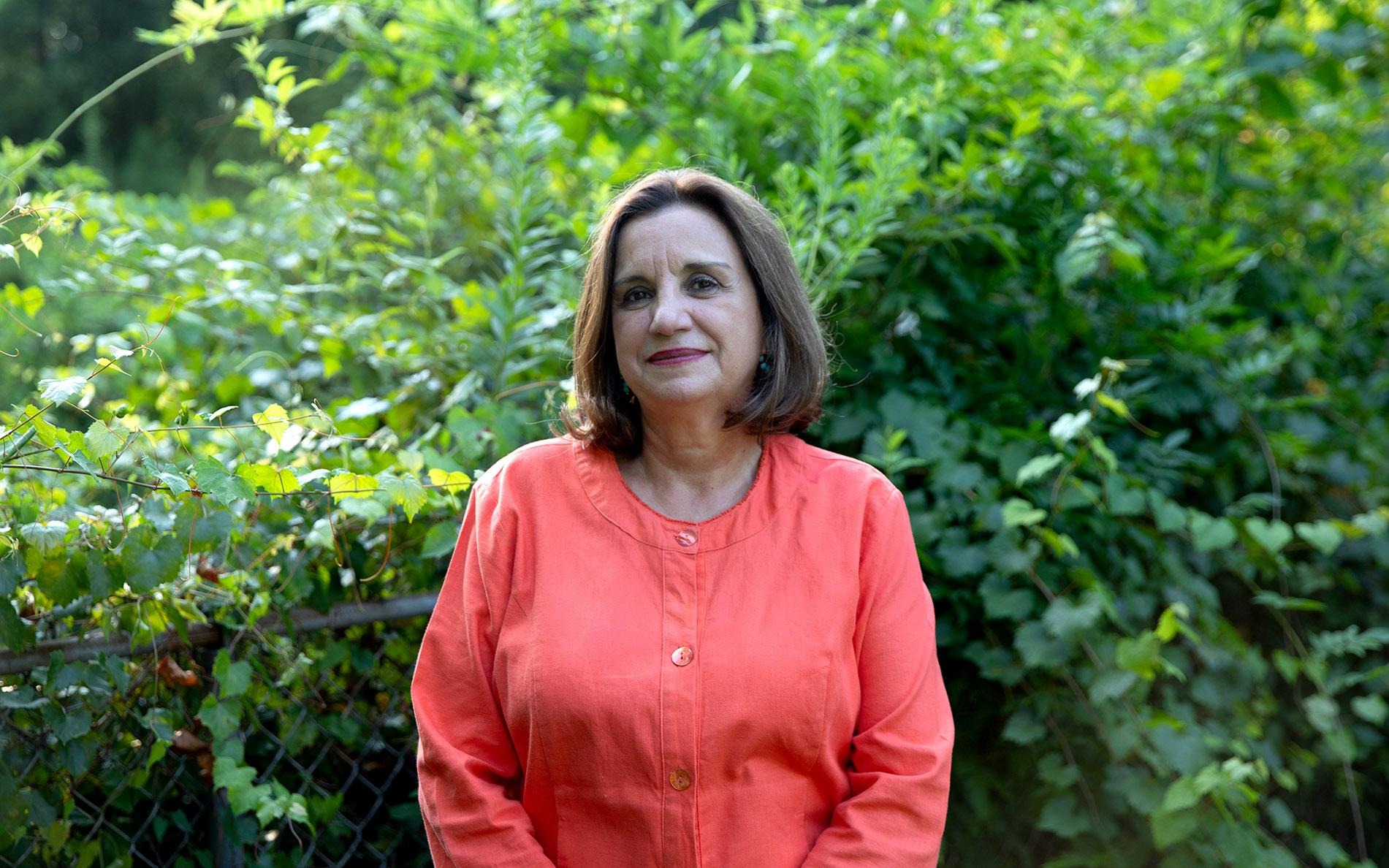 Isabel Scarinci standing outdoors in front of dense green foliage.