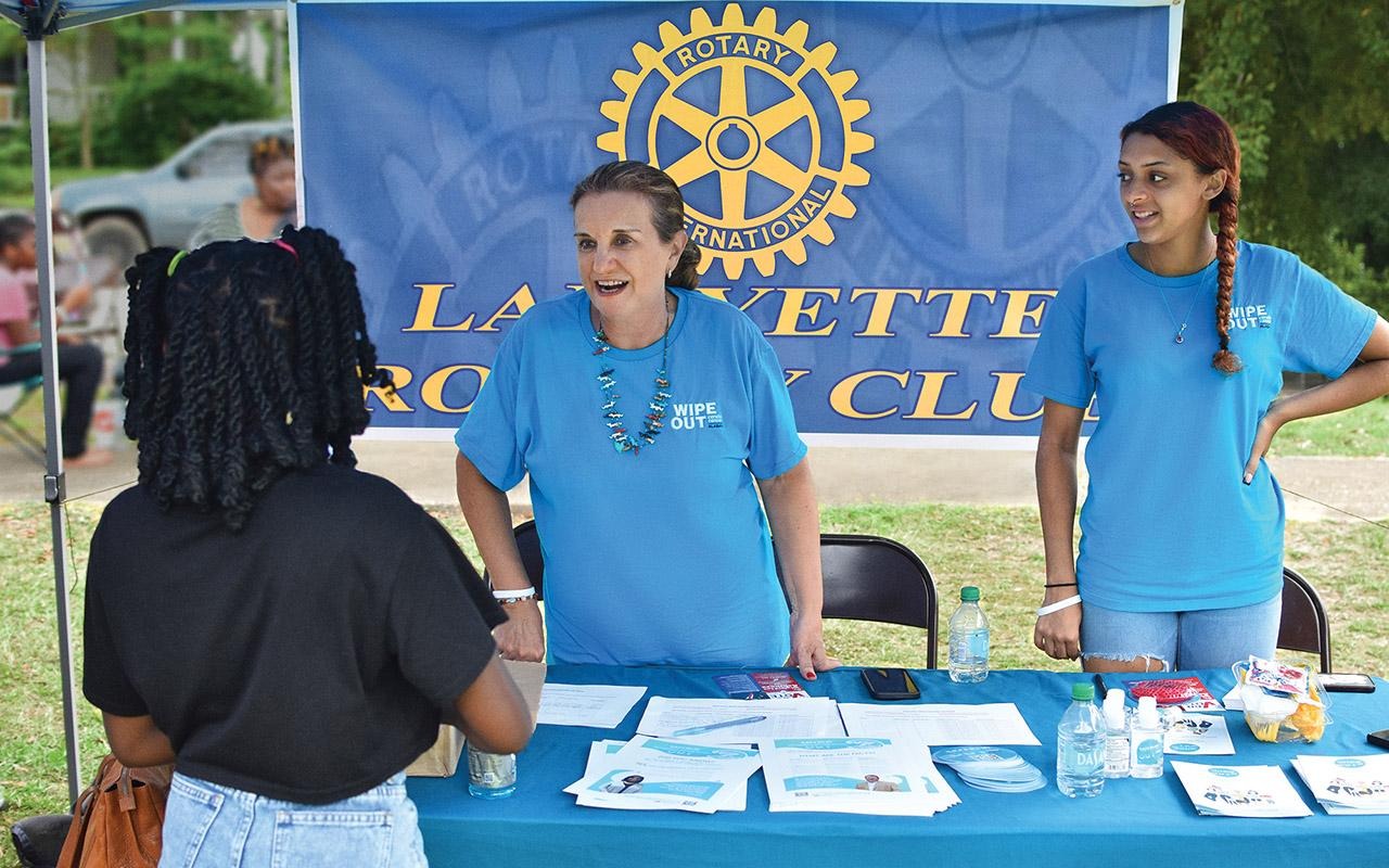 Volunteer speaking with a visitor at a Rotary International Lafayette Rotary Club information table at an Operation Wipe Out event.