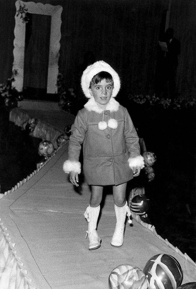 Isabel Scarinci as a child walking on a runway with a fur-trimmed coat and hat.