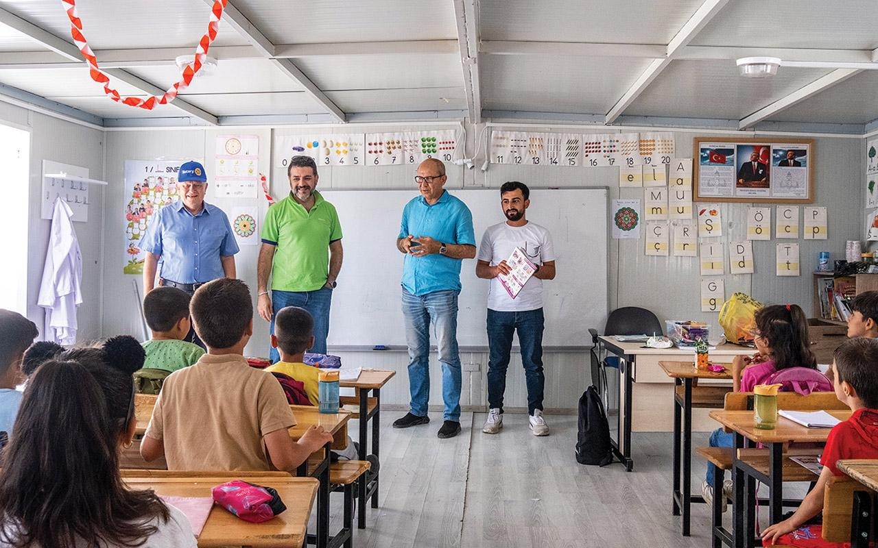 Rotary members Baysan, Öztürk, and Binzet speaking to students seated at desks in a classroom.