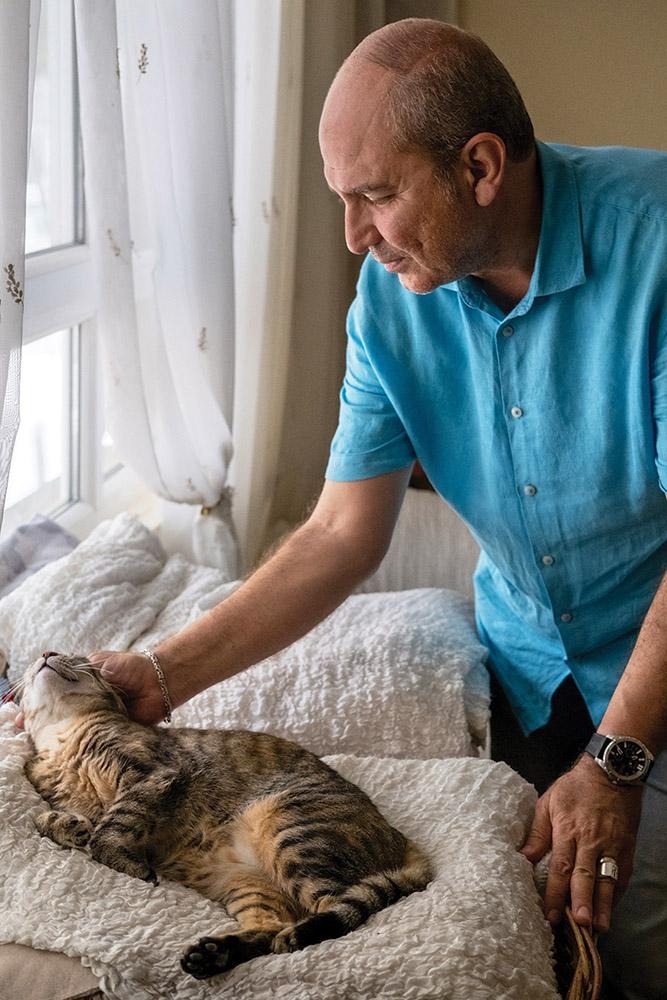 Rotary member Binzet petting a cat resting on a bed near a window.