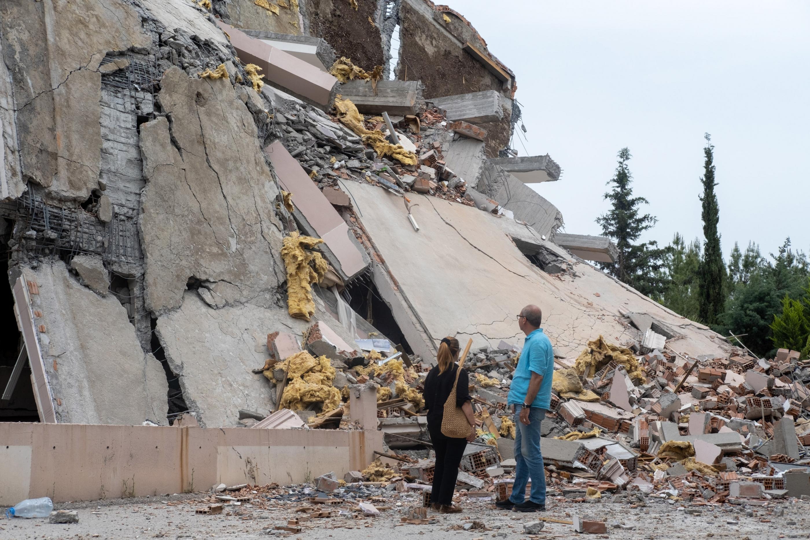 Two people standing beside the rubble of a collapsed building in Turkey.