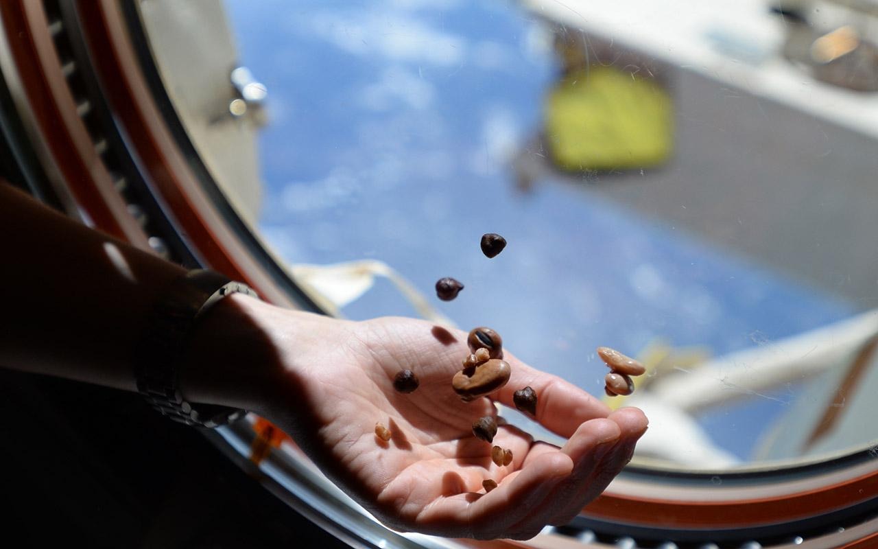 Granos de café flotando sobre una mano cerca de la ventanilla de una nave espacial.
