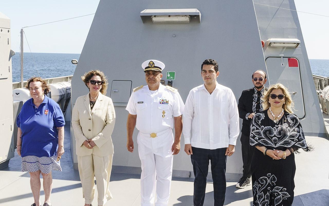 Several Rotary members joined government and navy officials walk beside a gray ship on a dock.