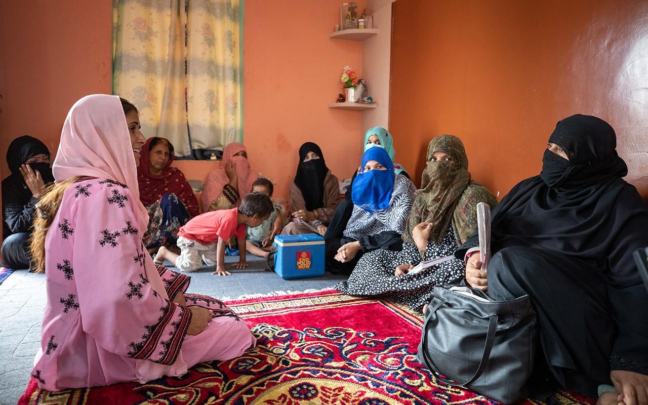 Lokale/e Gesundheitshelfer/innen in Pakistan sitzen auf einem gemusterten Teppich in einem Raum und nehmen an einer Gruppendiskussion teil.