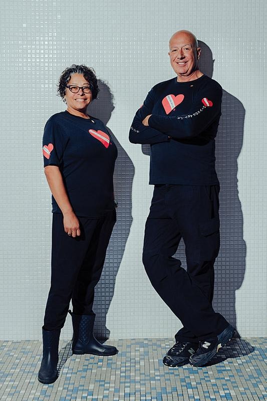Rotary members Tinamarie Hernandez and Jim Elliott standing against a tiled wall wearing matching shirts with heart logos.