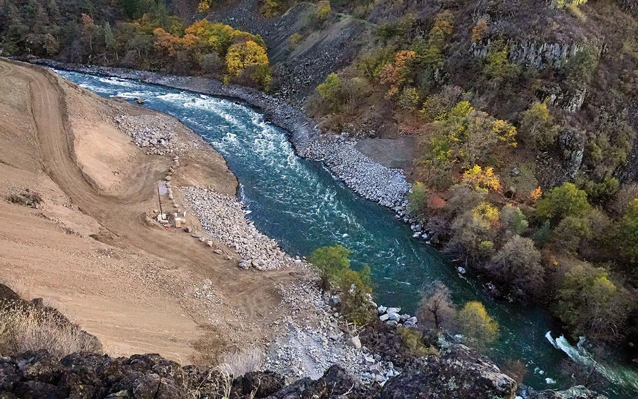 Aerial view of the Klamath River winding through a rocky valley beside a large earthwork excavation.