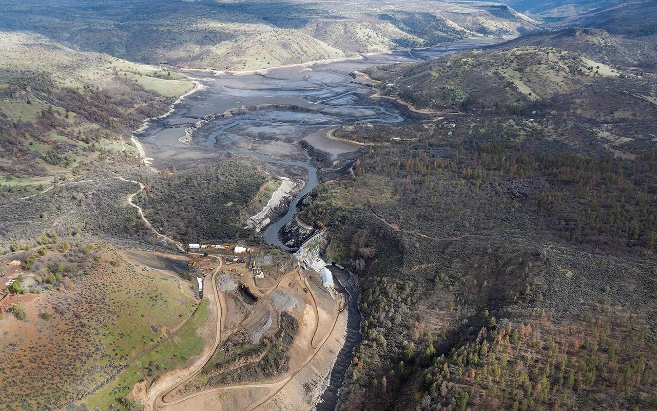Aerial view of a river valley with earthwork excavation, roadway, and bridge surrounded by rolling hills.