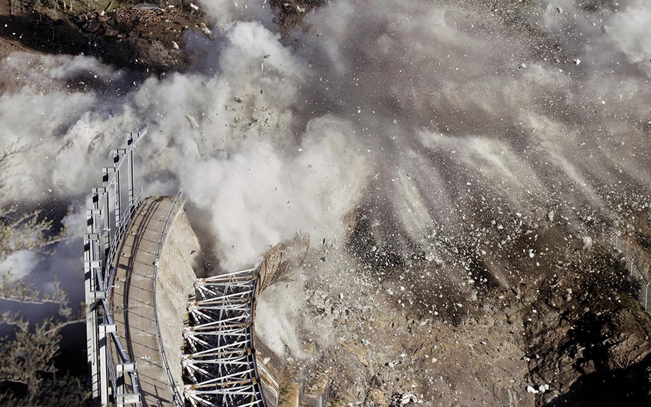 Aerial view of a dam releasing water and sediment into a river channel during demolition.