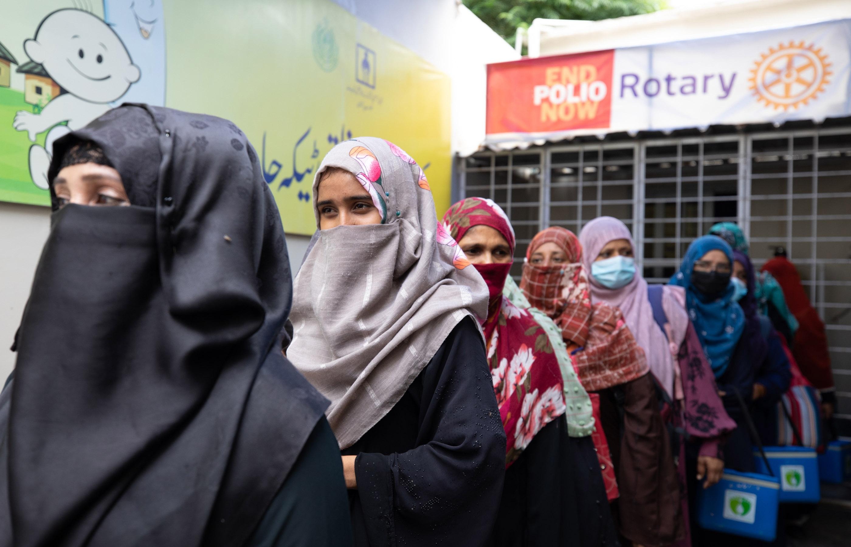 Persone in fila fuori da una clinica sotto cartelli con le scritte "End Polio Now" e "Rotary"