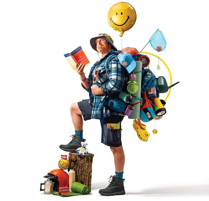 Person carrying a backpack overflowing with toys, books, blocks, and a jump rope beneath a smiley balloon