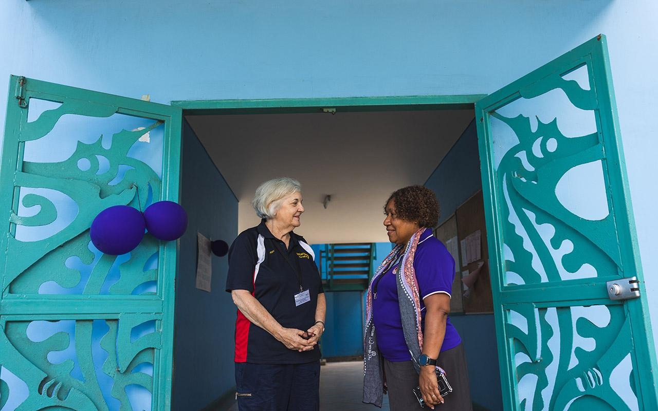 Judith Brown (à gauche), organisatrice de l'atelier et membre du Rotary club de Morialta, en Australie-Méridionale, en conversation avec Mary Sitaing, dans l'embrasure d'une porte ornée de portes décoratives de couleur turquoise, avec des ballons violets à proximité