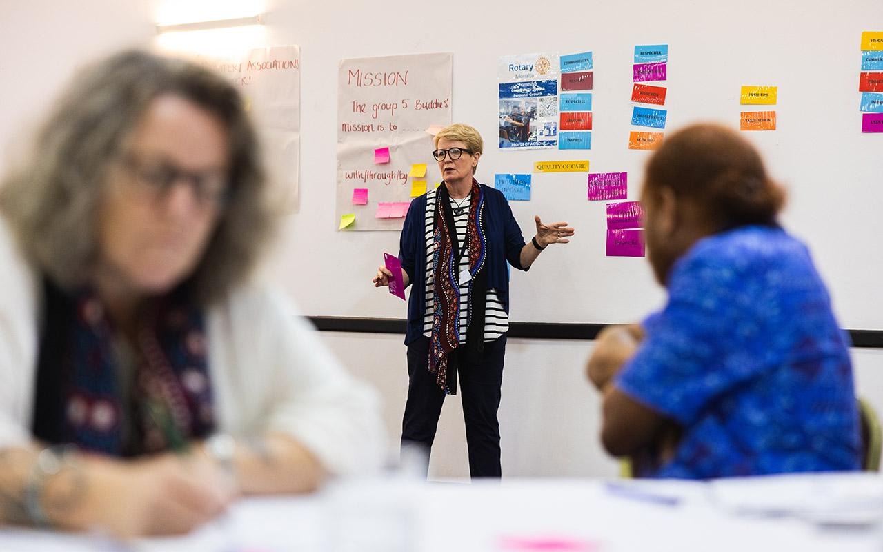 Person presenting beside a whiteboard with multicolored sticky notes while two participants sit in the foreground
