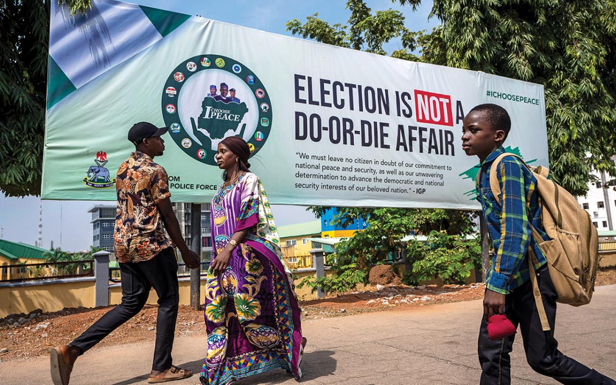 Pedestrians in Abuja walk past a banner from the police force carrying a message calling for peace during the elections.
