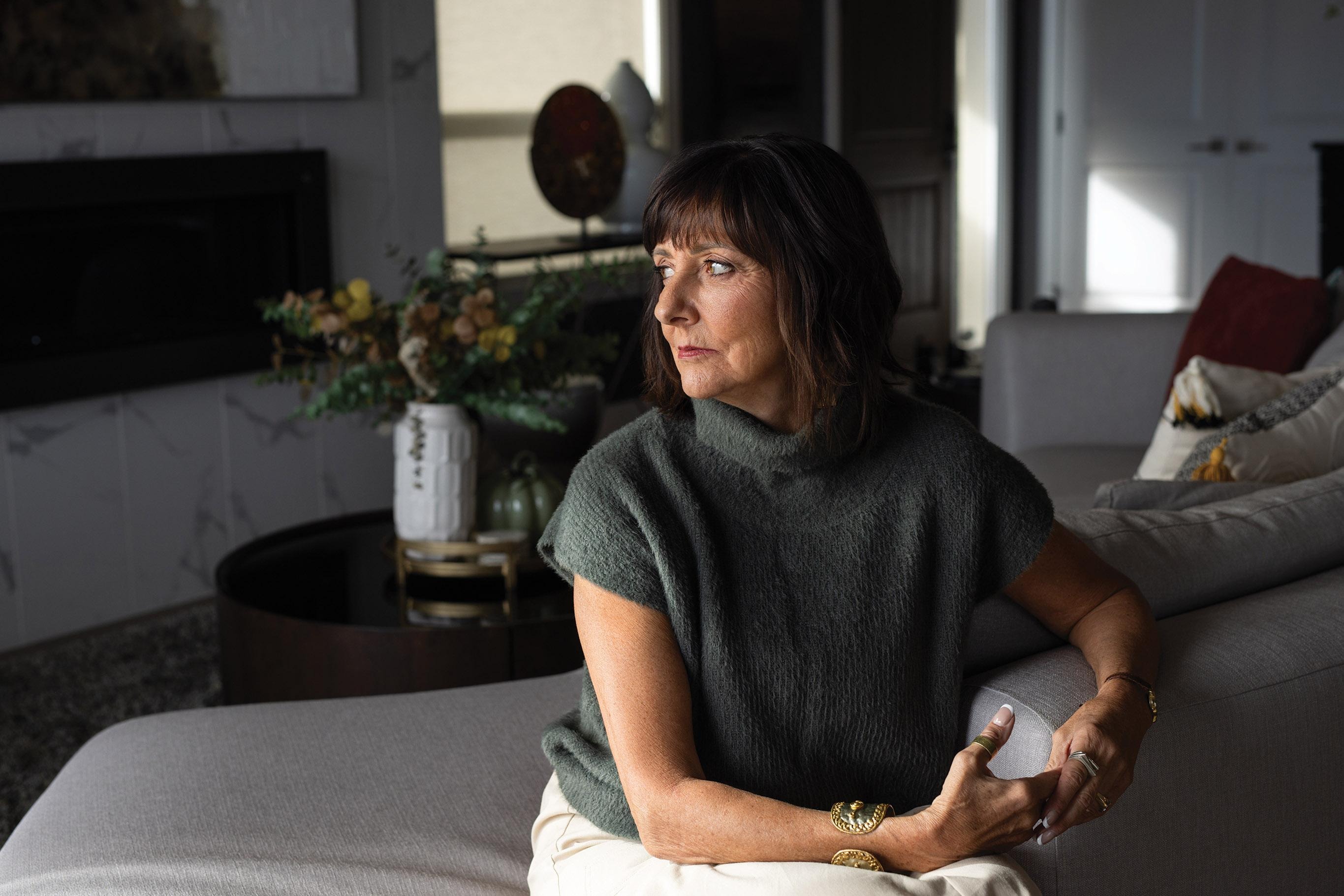 Julie Mulligan sitting on a bed holding a baby while looking toward a window in a softly lit room