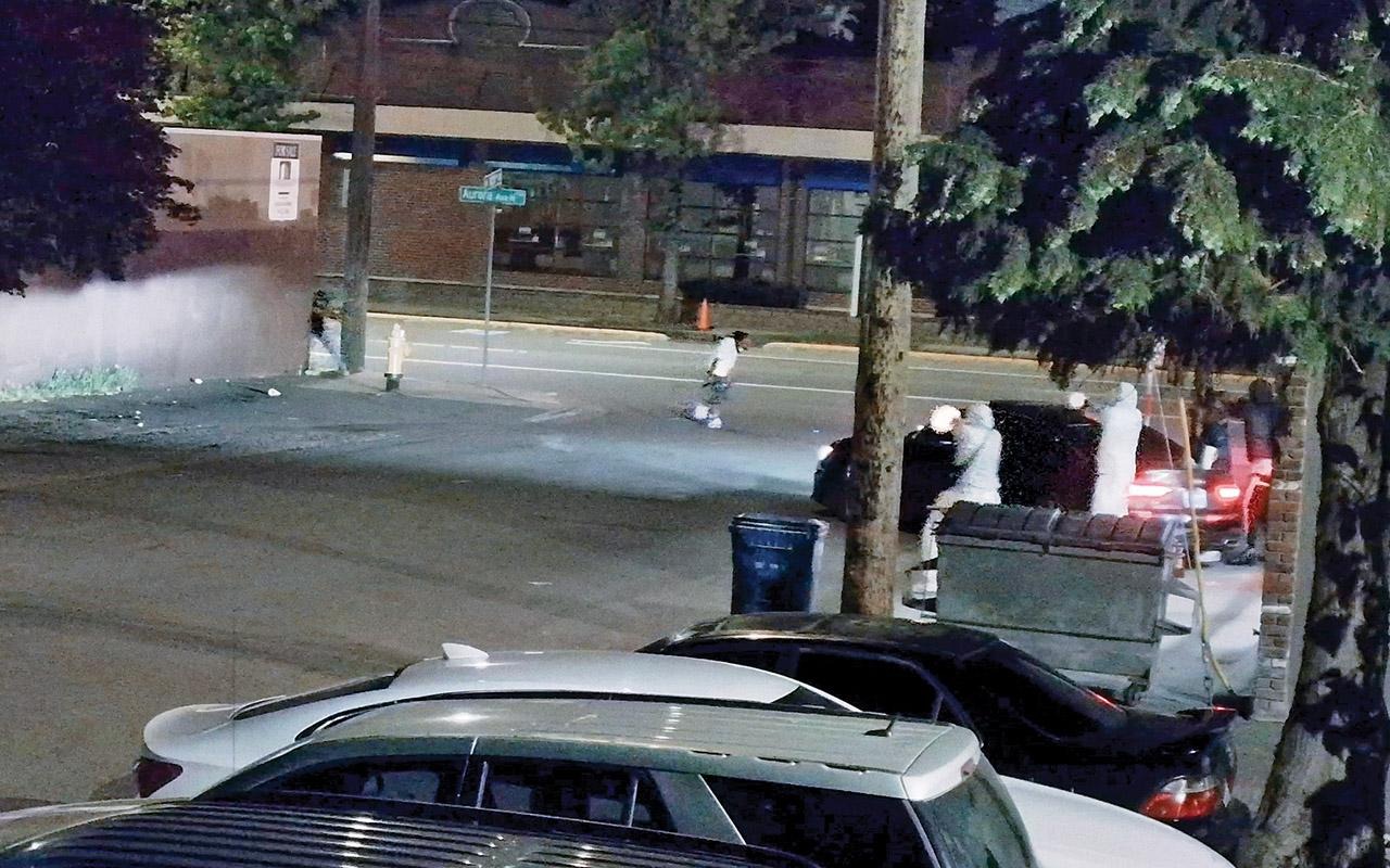 Parked cars along a street at night, with a person standing beside a vehicle under streetlights.