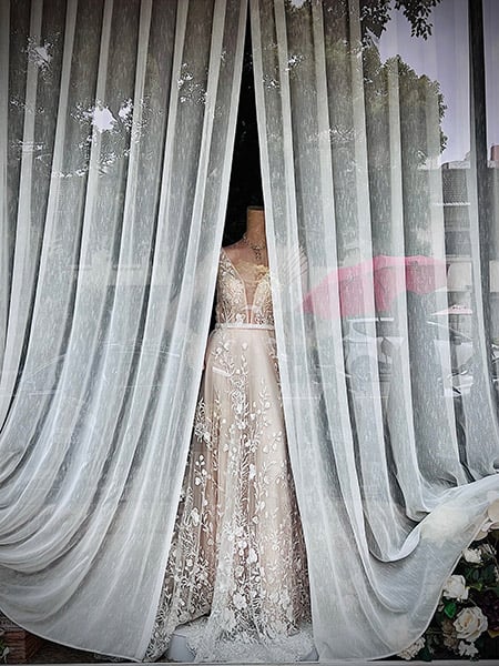 Una donna con un ombrello rosa passa davanti alla vetrina di un negozio dove è esposto un abito da sposa