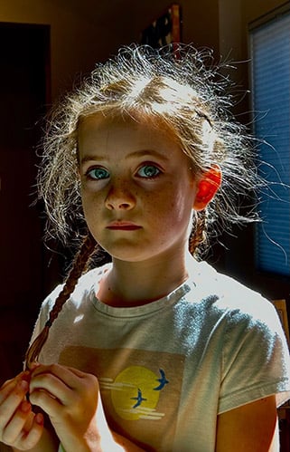 Willa Talbot, una bambina di sette anni, tiene in mano un filo, illuminata dalla luce del sole che entra da una finestra lì vicino.