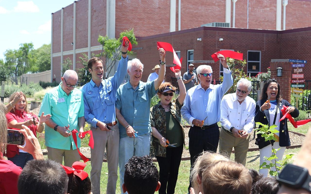 People cutting a red ribbon during a dedication ceremony outside a brick building.