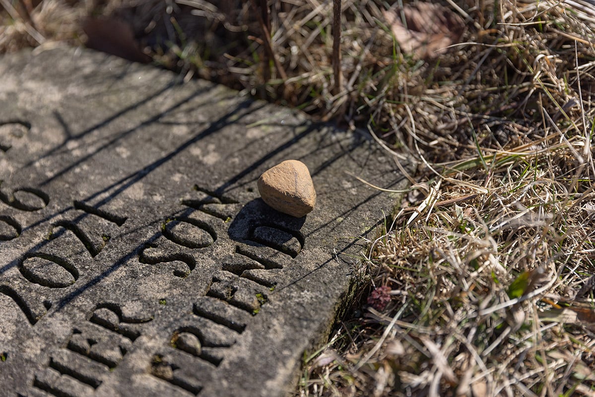 Gravestone with the visible text “Not for their merit” and a small stone resting on top.