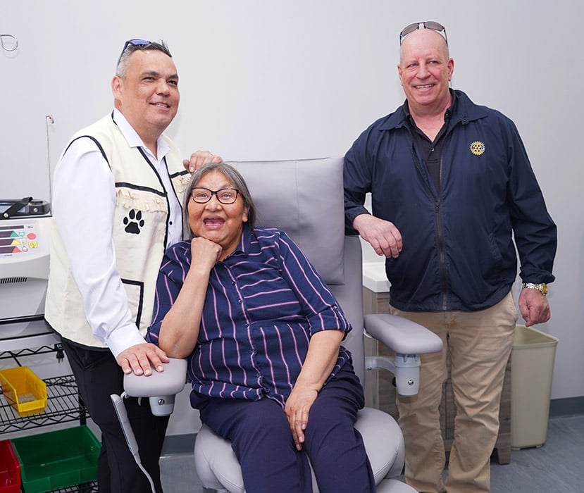 Acompañantes posando en un consultorio junto a un paciente sentado, cerca de una silla de examen médico.