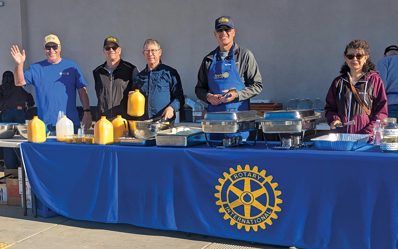 rotary members standing behind a table with serving trays and a Rotary logo tablecloth.