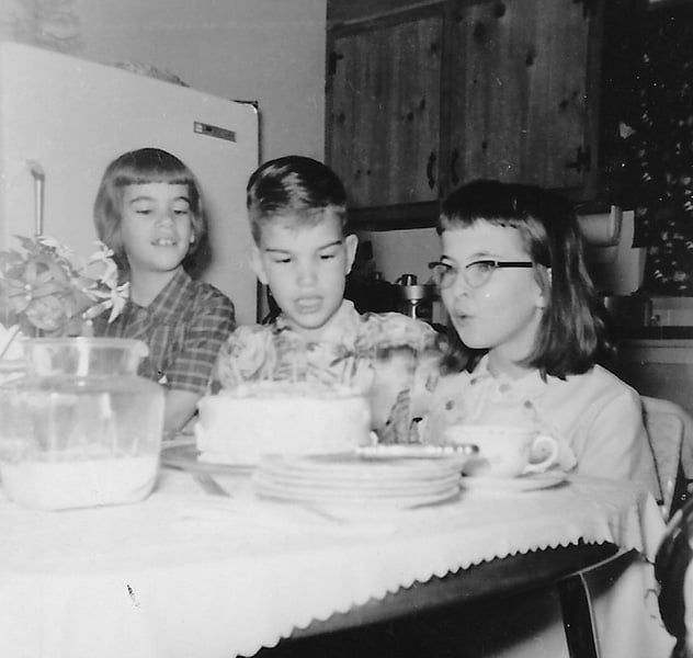 Siblings watch their sister blow out the candles on her birthday cake.