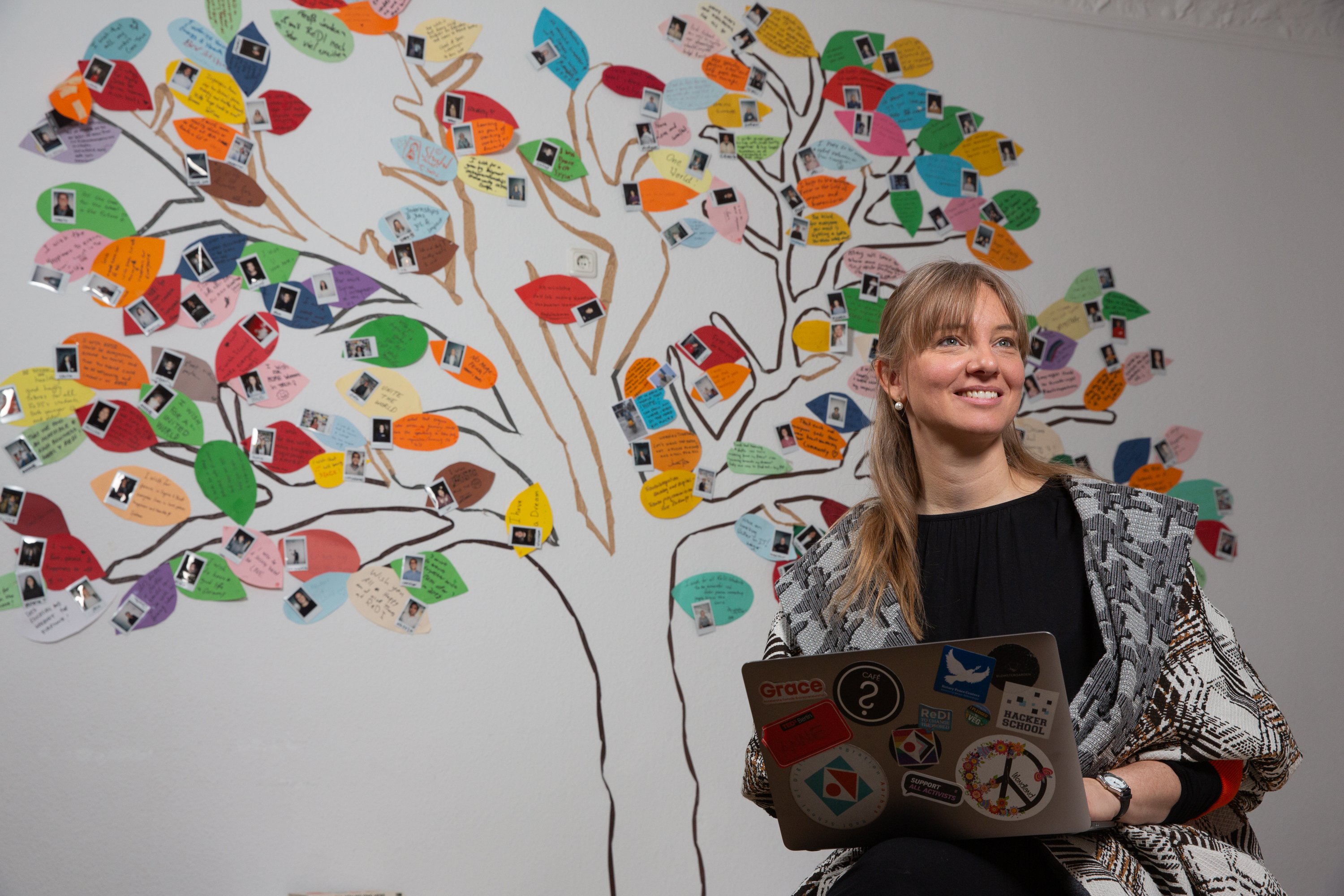 Anne K. Bathel, a Rotary Peace Fellow, sits in front of a mural holding a laptop.