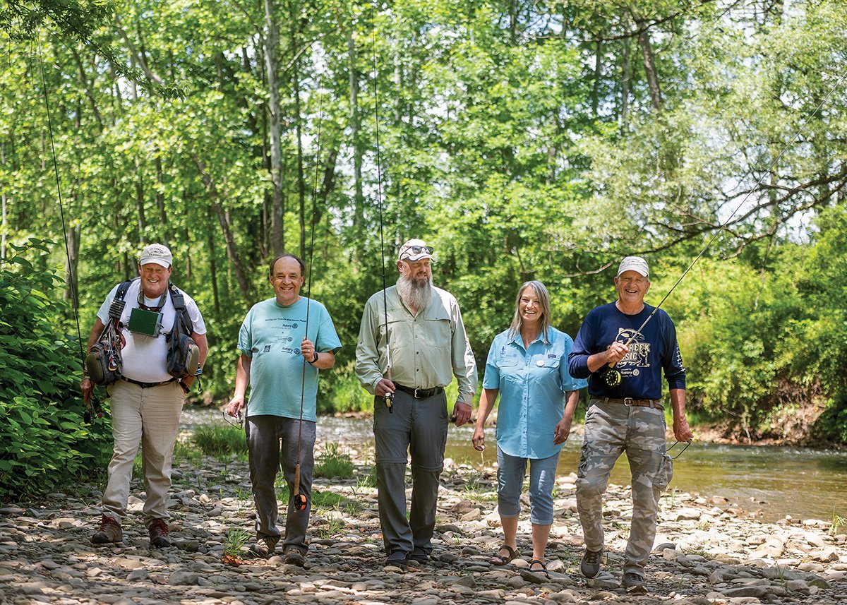 People stand outdoors with fishing gear to participate in a fly-fishing tournament