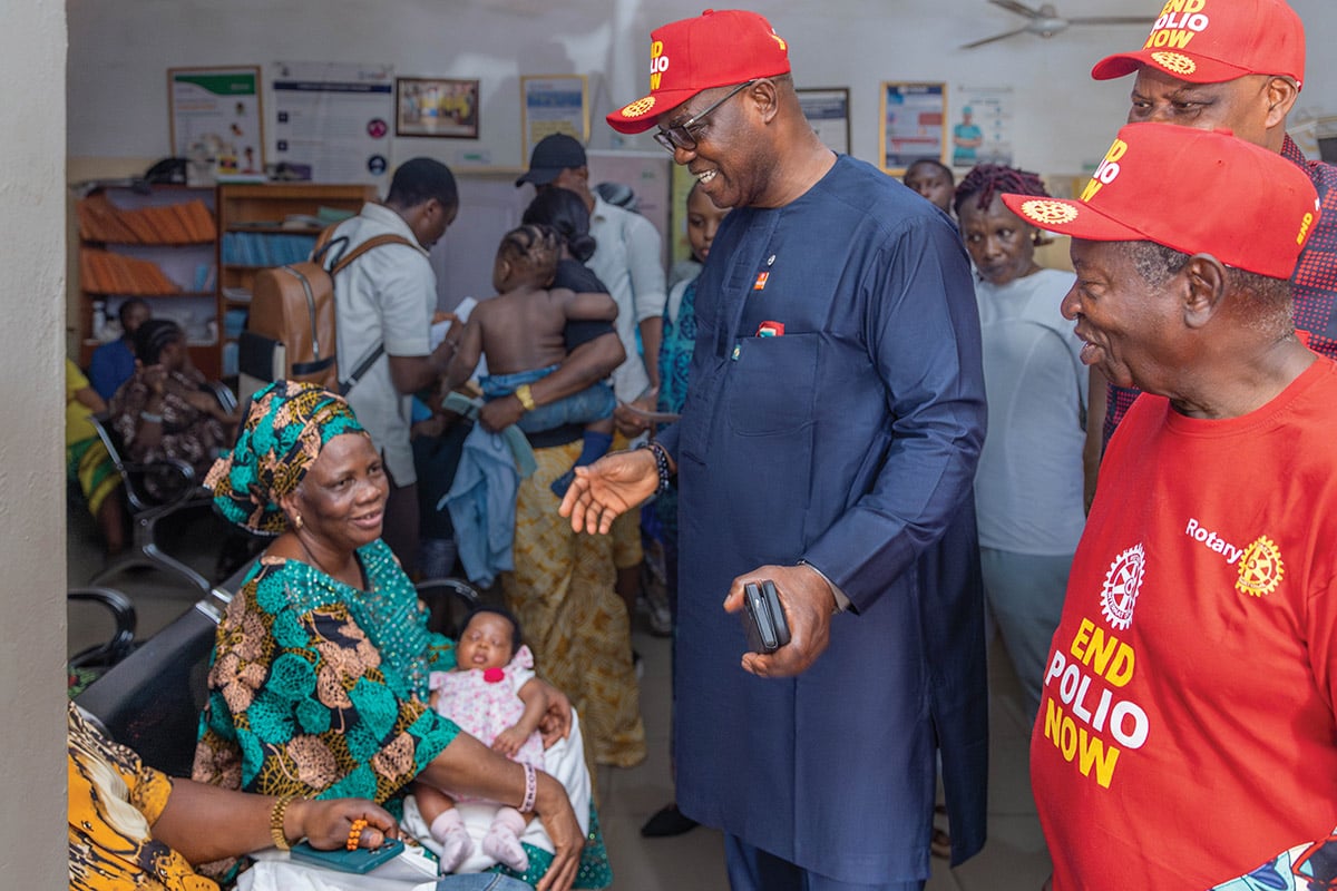 ババローラさんと、「End Polio Now」のキャップをかぶった人々が、診療所の待合室で、お子さん連れのご家族を訪ねています。 