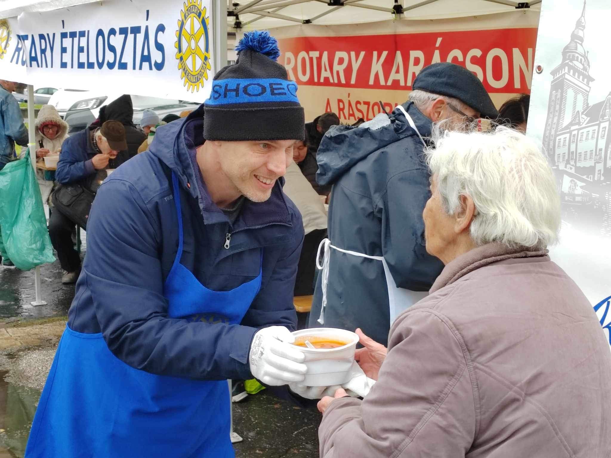 Volunteer handing a cup to an older adult at an outdoor meal distribution event.