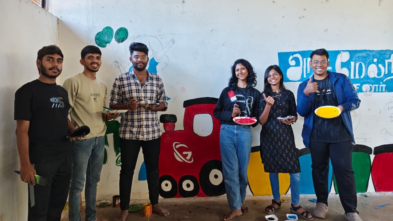 Group of people standing beside a painted train mural, with one person holding a plaque in an indoor community space.