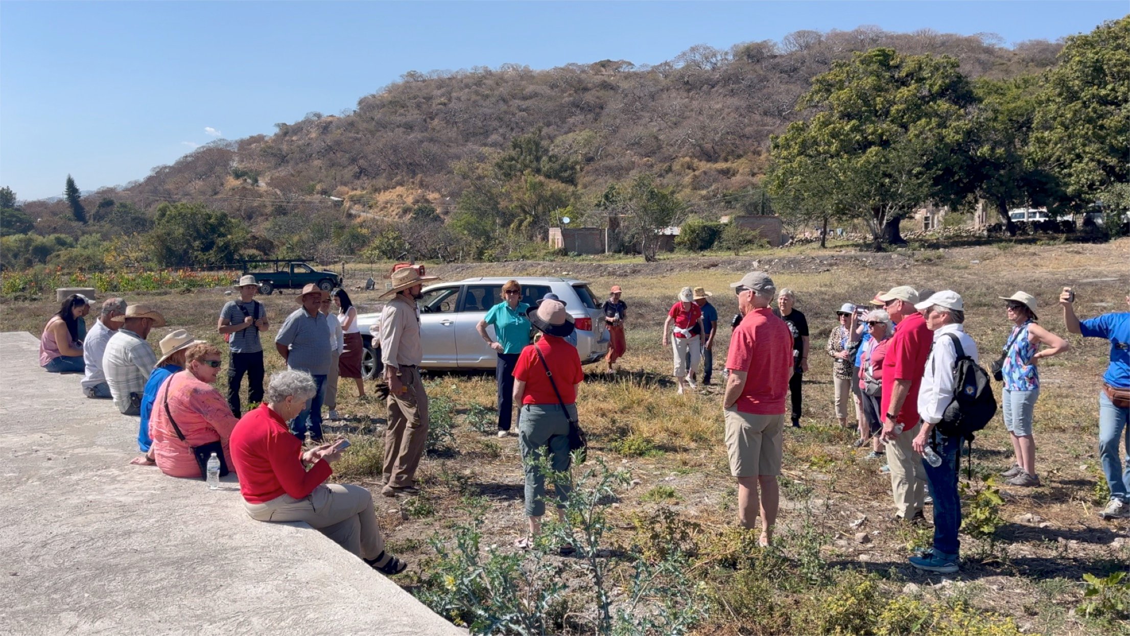 People gathered in a field during an outdoor service project, with hills and trees in the background.